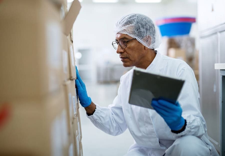 Worker wearing gloves and a hairnet inspecting boxes with a tablet in a warehouse