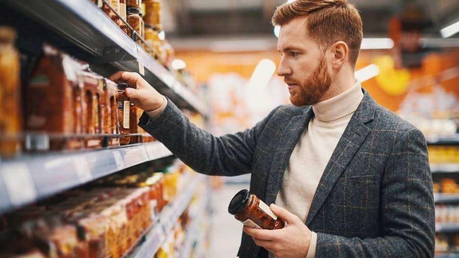 Man selecting a jarred product from a grocery store shelf