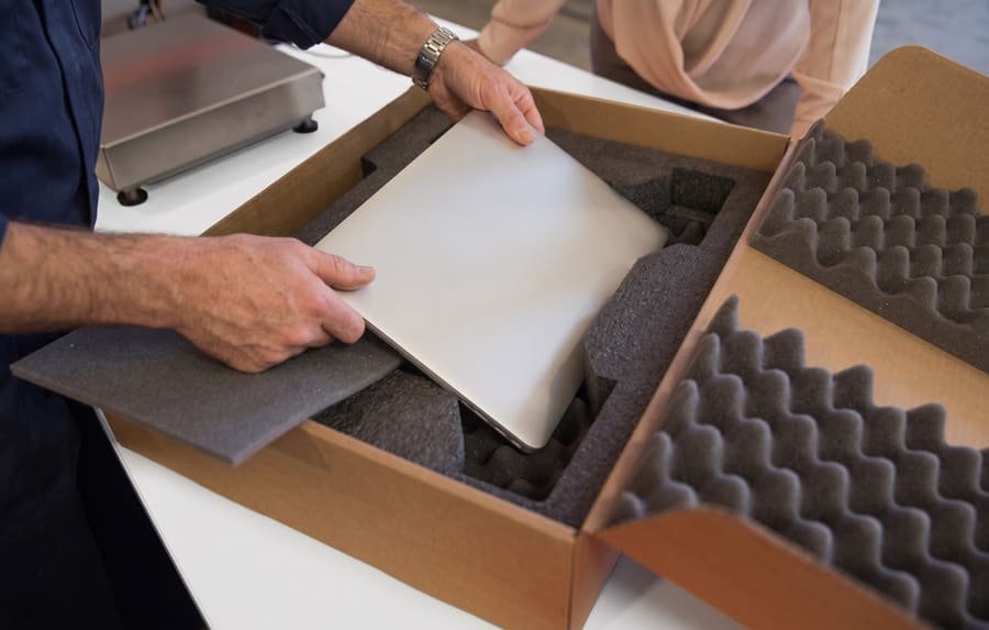 Hands packing a laptop into a foam-lined shipping box