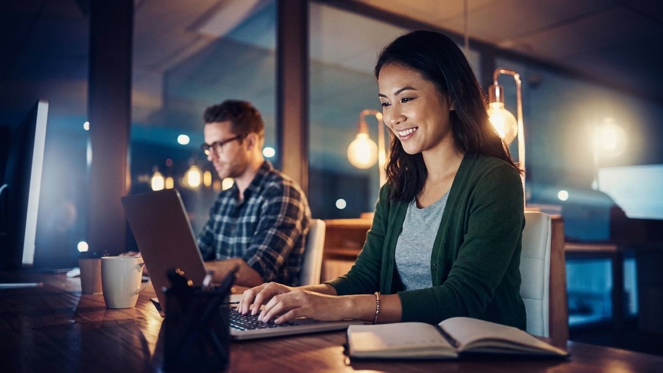 Woman smiling while working on a laptop in a co-working space at night